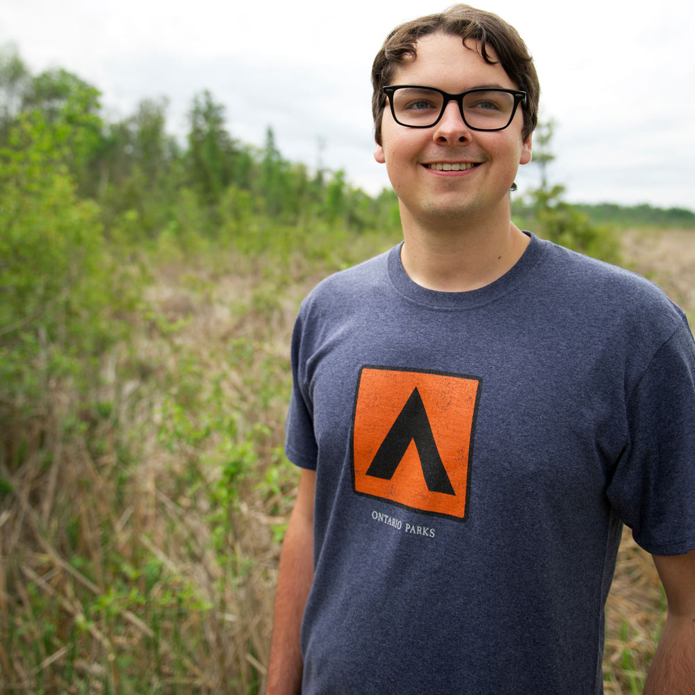 Man wearing Unisex heathered navy Park Icon Tent T-shirt, featuring an orange and black tent graphic in a black square on centre chest.